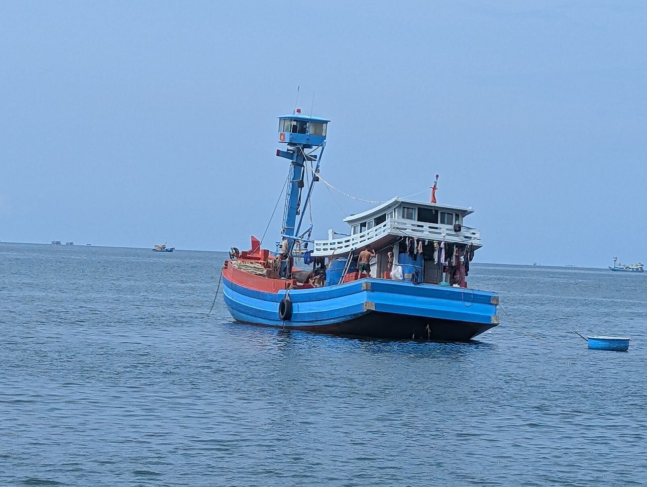 Ein blau gestrichenes vietnamesisches Fischerboot mit Nationalflagge liegt vor der Küste, ein Besatzungsmitglied an Deck